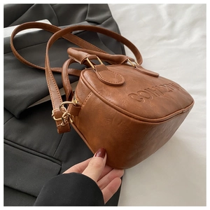 Detail showing the embossed COHLDK logo and gold hardware on brown leather bag
