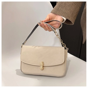 Detail of a beige baguette bag showing a unique golden peanut-shaped metal clasp