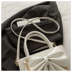 Détail du sac en similicuir blanc avec un grand nœud et une bandoulière en chaîne dorée