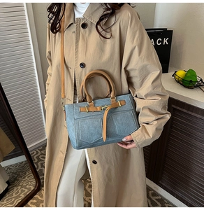 Detailed shot of blue denim shoulder bag featuring brown leather handles and metal buckles