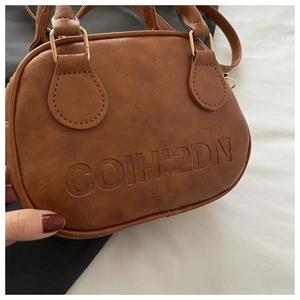 Close-up of brown litchi pattern leather bag showing embossed lettering and gold hardware
