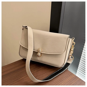 Close-up of cream shoulder bag featuring a unique gold peanut-shaped metal lock closure