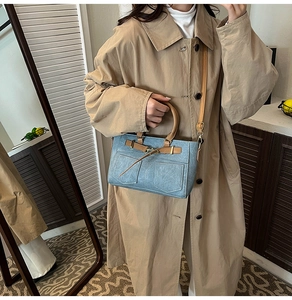 Detail of light blue denim texture handbag with brown leather straps and gold buckles