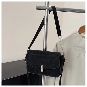 Detail of a black square bag featuring a unique peanut-shaped metal lock and gold chain strap