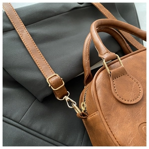 Macro detail of brown retro leather handbag featuring golden metal hooks and fine textures