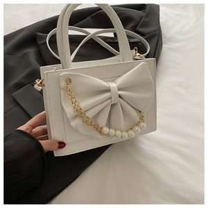 Détail d'un sac à main blanc avec un grand nœud 3D, une chaîne dorée et des perles chic