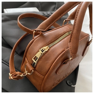 Detailed close-up of brown leather bowling bag with gold zipper and embossed texture