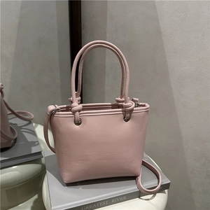 Rosafarbene Trapez-Beuteltasche mit Knotengriffen und Umhängegurt auf grauem Grund