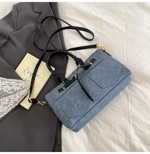 Detail of blue denim shoulder bag with dual front pockets and gold-tone hardware on grey blazer