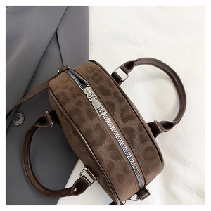 Detail view of dark brown leopard print circular handbag with silver zipper and round handles