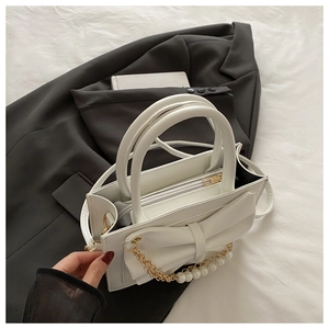 Détail d'un sac à main blanc avec grand nœud et accessoire chic en chaîne de perles
