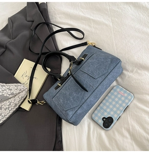 Detail of blue denim textured handbag with black handles and golden metal hardware