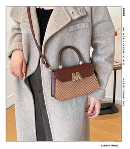 Détail du sac bandoulière avec rabat en cuir marron et texture tissée avec logo M doré