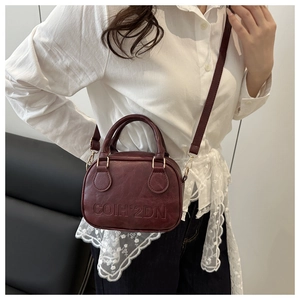 Detail view of burgundy leather handbag with embossed letters and gold metal hardware