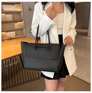Dettaglio di una grande borsa tote in pelle nera con patta su una scrivania in legno