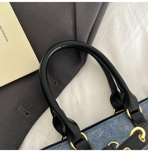 Detail of blue denim handbag with black leather circular handle and gold hardware accents