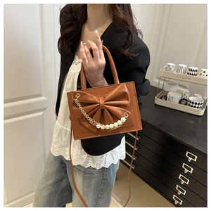 Gros plan d'un sac marron avec nœud, perles et chaîne dorée porté par un mannequin
