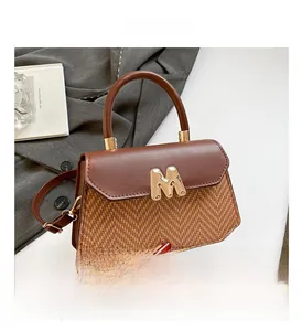 Detail of contrast stitch handbag with herringbone texture and gold metallic M logo