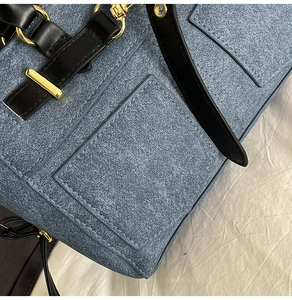 Detail of blue denim fabric texture and black leather strap with gold buckle on shoulder bag