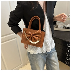 Détail d'un sac à bandoulière marron avec un grand nœud et une chaîne de perles