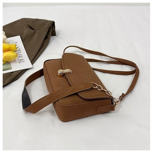 Detail of a brown shoulder bag featuring a unique golden peanut buckle and chain strap