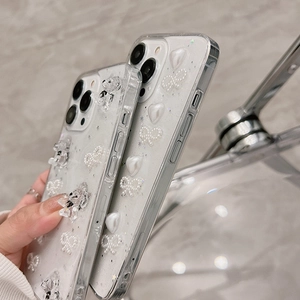 Détail d'une coque iPhone transparente avec cœur perlé, nœud et ours en paillettes 3D