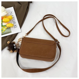 Detail view of brown pebbled leather shoulder bag with plush charm and two strap options