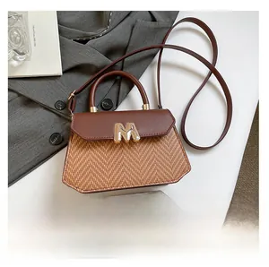Detail of woven texture handbag with brown leather flap and gold M hardware buckle