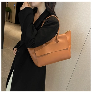 Dettaglio della borsa tote in pelle marrone con patta indossata da una modella in un corridoio