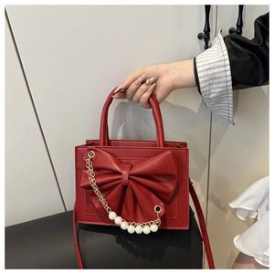 Détail d'un sac à main rouge avec grand nœud décoratif et chaîne en perles blanches