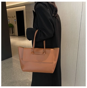 Side view of a large caramel leather tote bag worn by a model in a modern interior