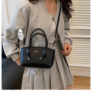 Détail du sac à main en cuir noir mat avec texte FASHION et nœuds décoratifs