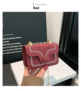 Detail of dark red crossbody bag featuring white embroidery and gold chain strap