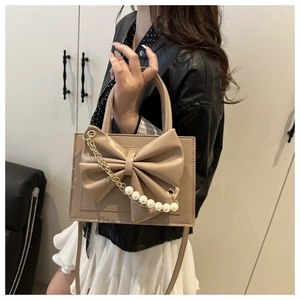 Détail d'un sac à main beige avec nœud 3D et chaîne de perles tenu par un mannequin