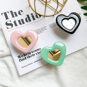 Three heart-shaped phone grips with mirrors in pink black and green on a magazine