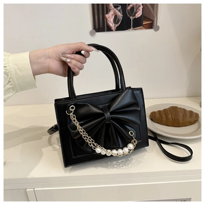 Détail d'un sac à main noir en simili cuir avec nœud géant et breloque en perles