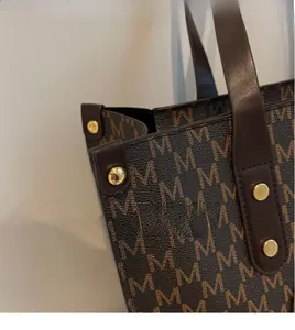 Detail of dark brown monogram tote bag with gold stud rivets and polished leather trim