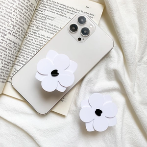 White flower cell phone grip with black heart detail on a white iPhone against a fabric background