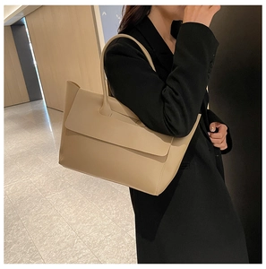 Dettaglio di una borsa tote beige indossata con un blazer nero per un look da ufficio