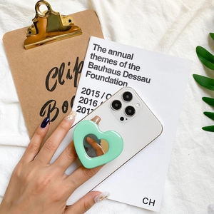 Close-up of a mint green heart-shaped phone socket mirror on a white smartphone