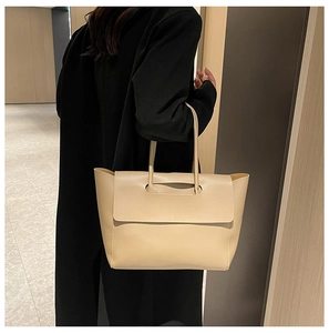 Close-up of beige tote bag showing textured leather material on a model in a black coat
