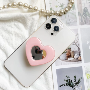 Pink heart-shaped telescopic phone grip with built-in mirror on a white smartphone