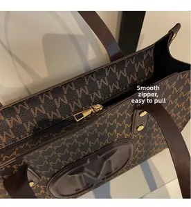 Detail view of smooth golden zipper and textured M-letter monogram on brown tote bag