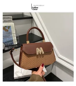 Detail of a brown woven crossbody bag featuring a golden M-letter buckle on white book