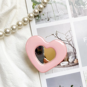 Detailed view of pink heart phone grip with built-in mirror on aesthetic fabric background