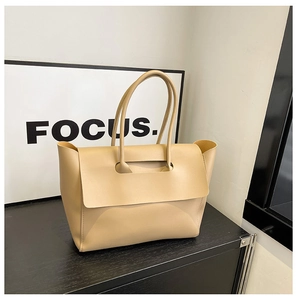 Dettaglio borsa shopper beige chiaro con patta grande e manici sottili su legno nero