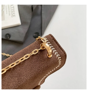 Detail of brown suede bag featuring gold chain strap and elegant white embroidery