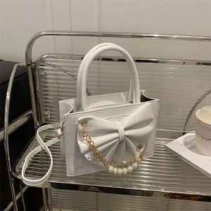 Sac à main en cuir blanc avec nœud, chaîne de perles et bandoulière sur étagère chic