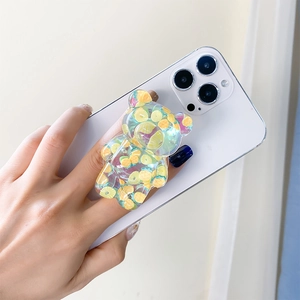 Detail of transparent bear phone grip with colorful fruit slices held by hand on white phone