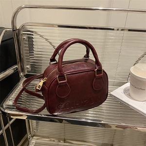 Vintage dark red leather mini Boston bag with embossed logo on a modern shelf display